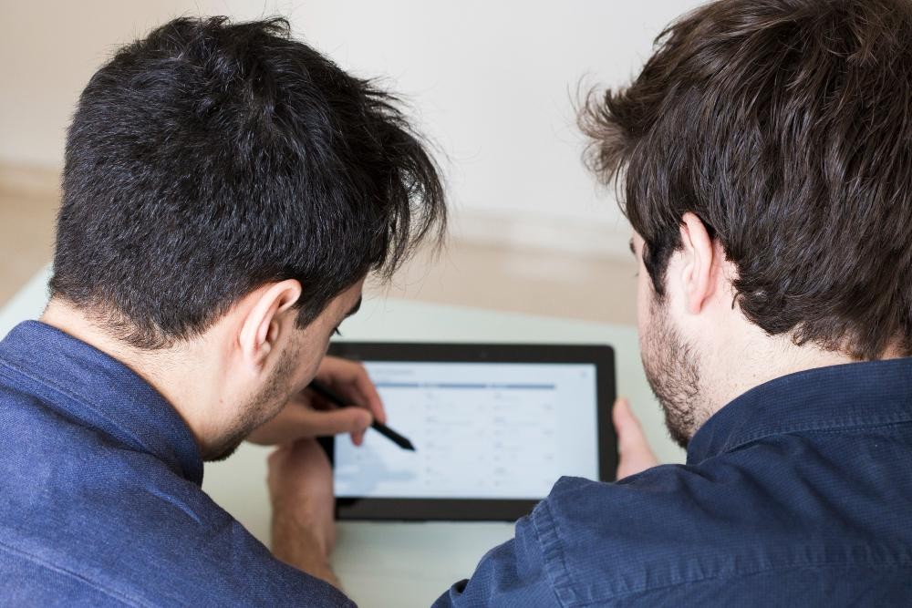 Two men collaborating while working on a tablet, viewed from behind.