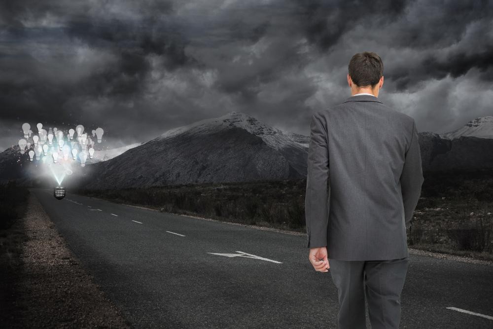 Businessman walking alone on a road toward glowing light bulbs under a stormy sky, symbolizing ideas and innovation.