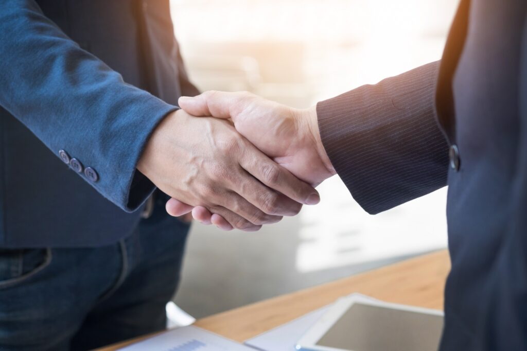 Close-up of two businessmen shaking hands over a desk with a digital tablet and documents.