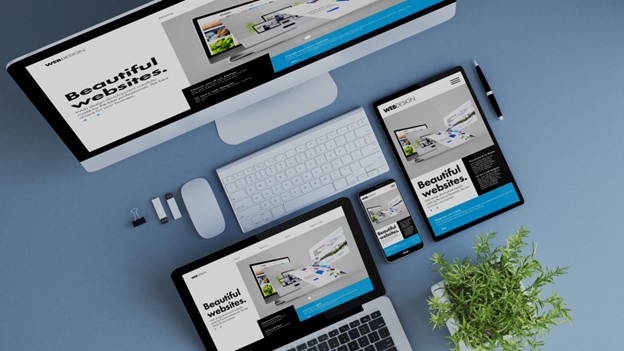 A desktop computer, tablet, and smartphone display the same website—showing Why Your Website Isn’t Just a Website; a keyboard, mouse, plant, and office supplies are arranged on a blue desk.